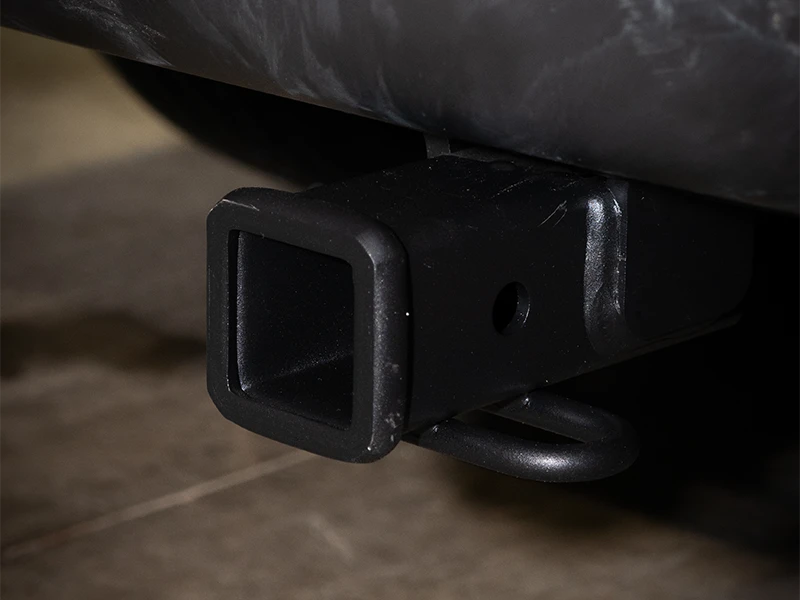 Close-up of a black trailer hitch receiver on a vehicle, with a metal loop underneath