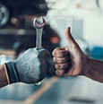 gloved hand holding a wrench fist-bumps a bare hand giving a thumbs-up
