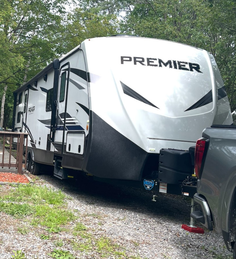 white Premier travel trailer hitched to a gray truck parked on a gravel driveway by trees