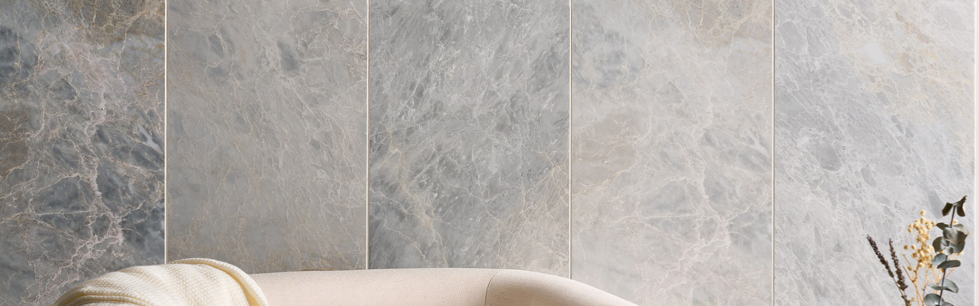 Close-up of a beige armchair and white blanket in front of a marble-patterned wall.