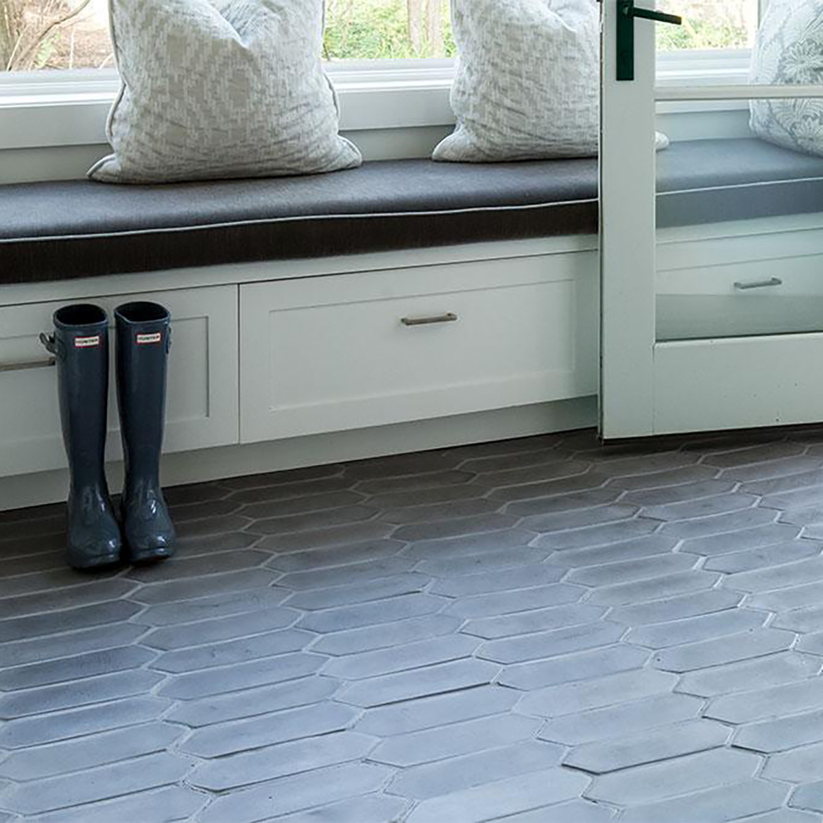 Gray tile flooring with rain boots and a seating area with pillows