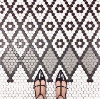 Person wearing black pointed shoes stands on hexagonal tile floor with a black and gray pattern.