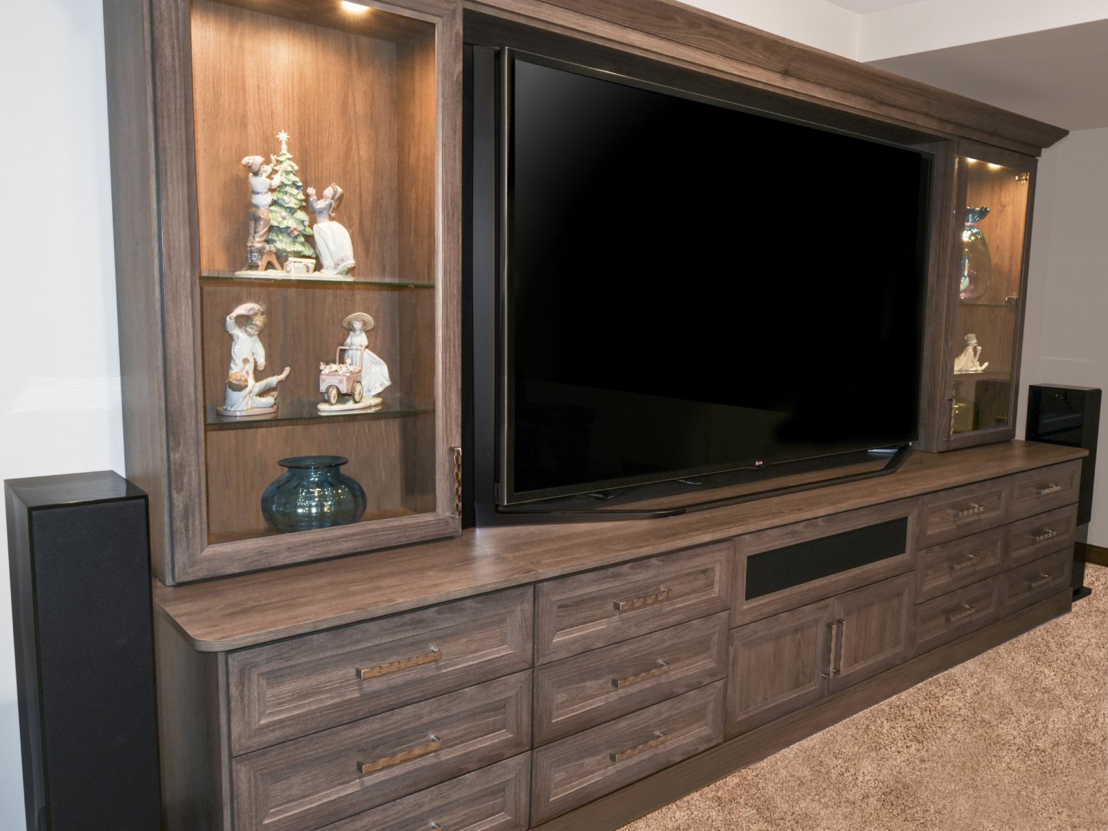 Built-in wooden entertainment center with a large TV and glass shelves displaying figurines.