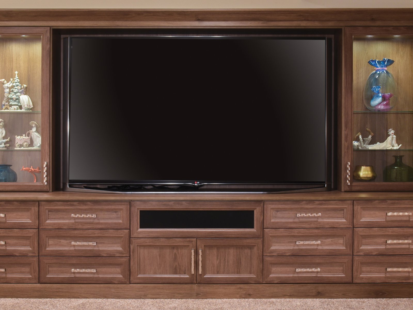 Large flat-screen TV in a wooden entertainment center with glass shelves and decorative items.