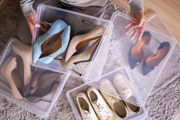 Person organizing high heels and shoes into clear plastic storage boxes on a carpeted floor.