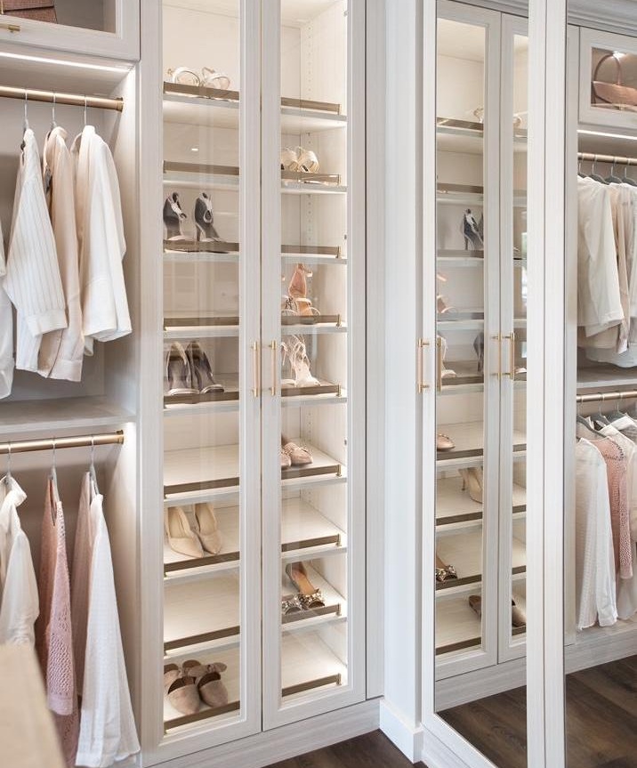Spacious walk-in closet with shelves of shoes and hanging white and pastel clothing.