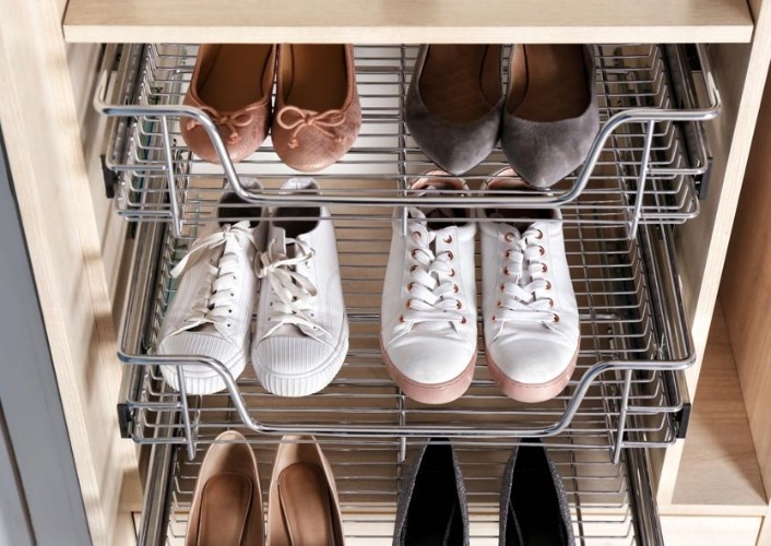 Three wire shoe racks in a closet hold pairs of sneakers, flats, and high heels.