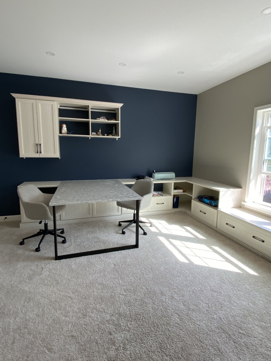 Home office with two chairs, built-in shelves, a deep blue accent wall, and a window seat.