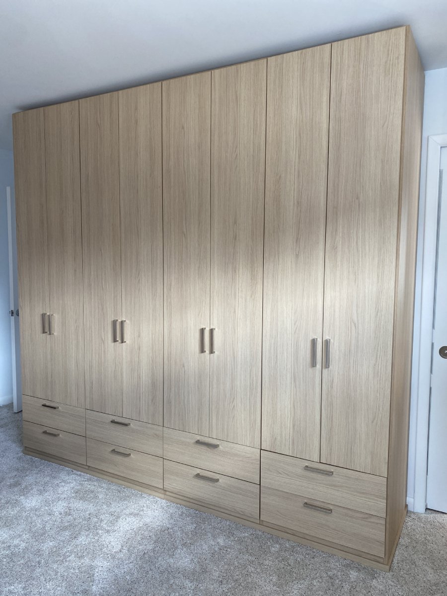 Large wooden wardrobe with six doors and six drawers, standing on a light carpeted floor.