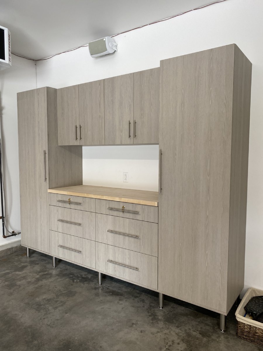 Light wood garage storage cabinets with metal handles and a countertop, on a concrete floor.