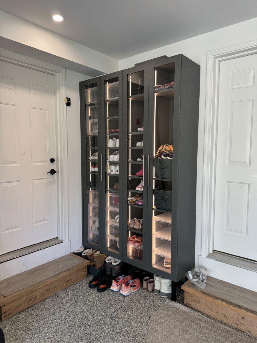 Tall glass-door shoe cabinet filled with shoes, next to white doors and wooden steps.