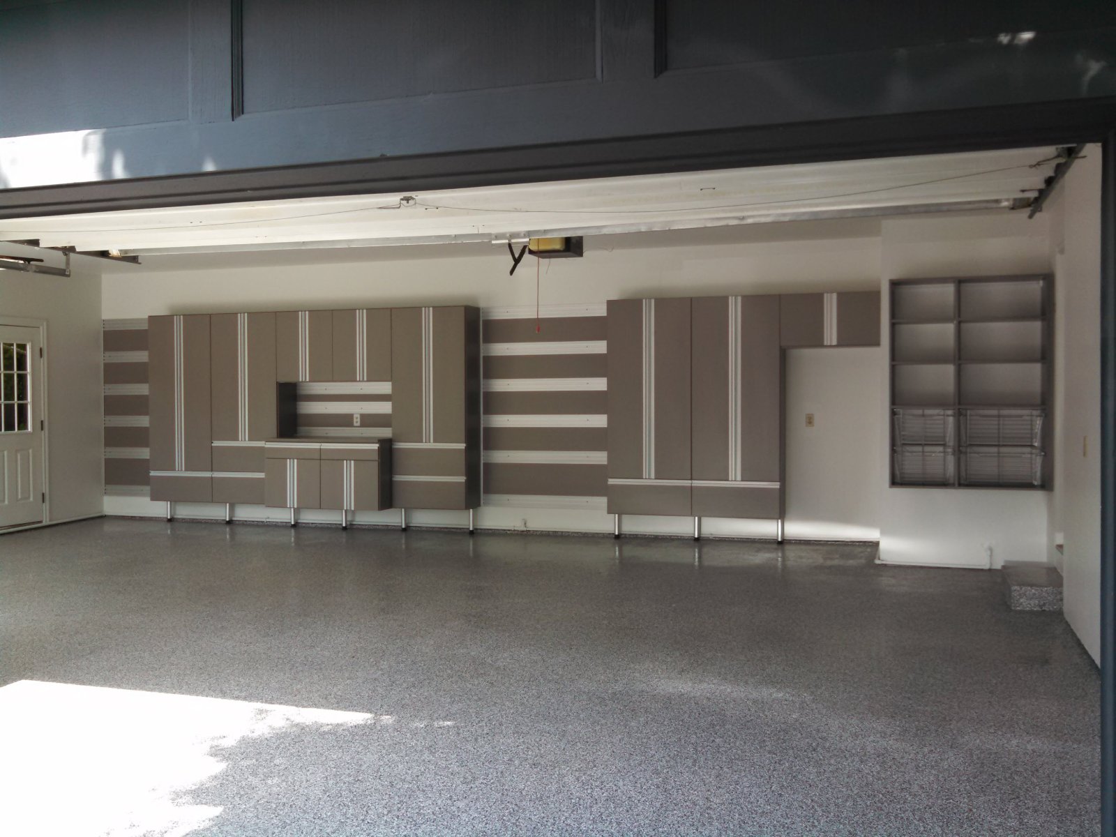A clean, empty garage with modern gray and white storage cabinets and shelves on the wall.