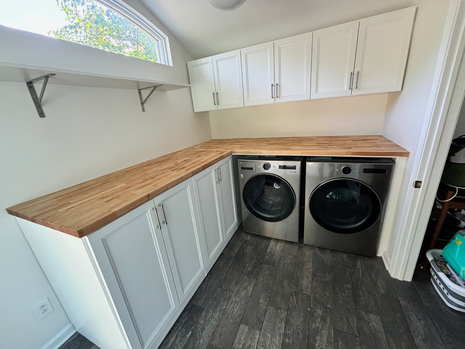 Modern laundry room with wood countertops, white cabinets, and stainless steel washer and dryer.