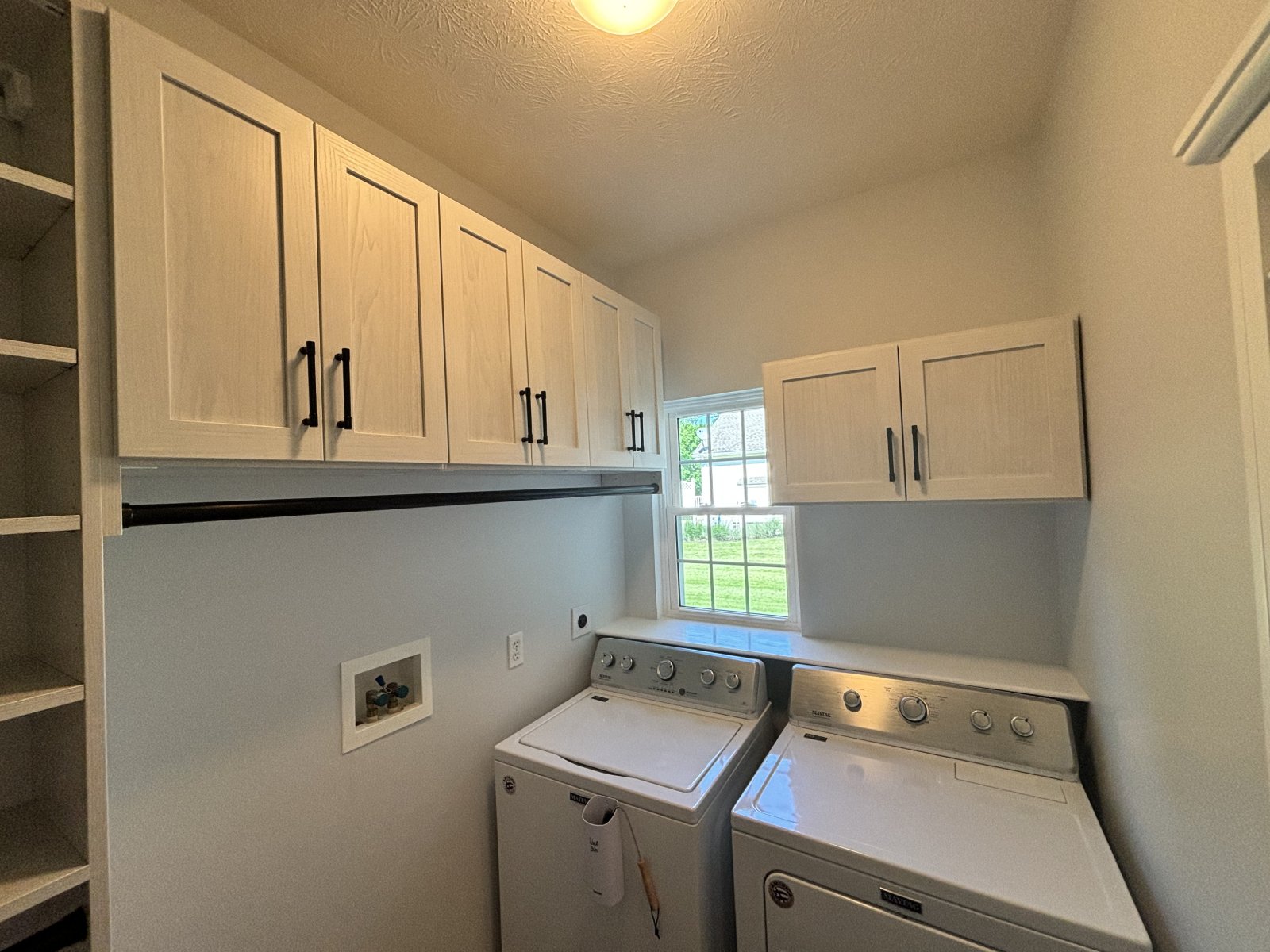 Laundry room with white cabinets above a washer and dryer, and a window letting in sunlight.