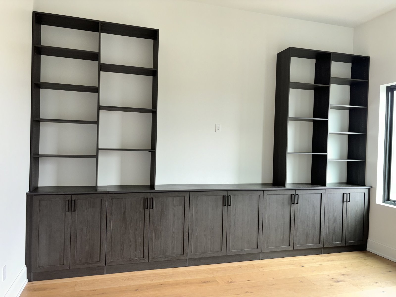 Dark wood built-in shelves and cabinets against a white wall with light wood flooring.