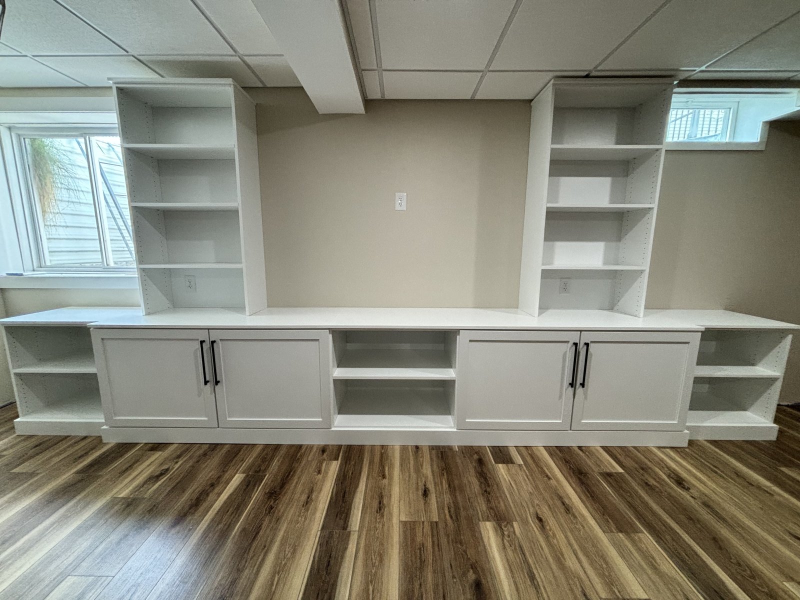 White built-in shelving unit with cabinets and open shelves against a beige wall on wood flooring.