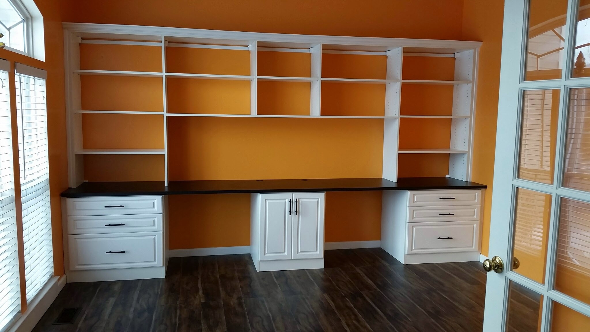 White built-in desk with shelves and drawers against an orange wall in a bright room.