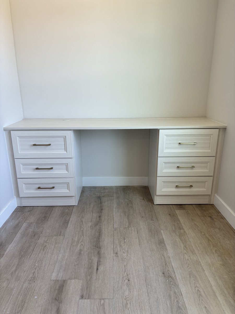 A white desk with six drawers, set against a light-colored wall and wood floor.