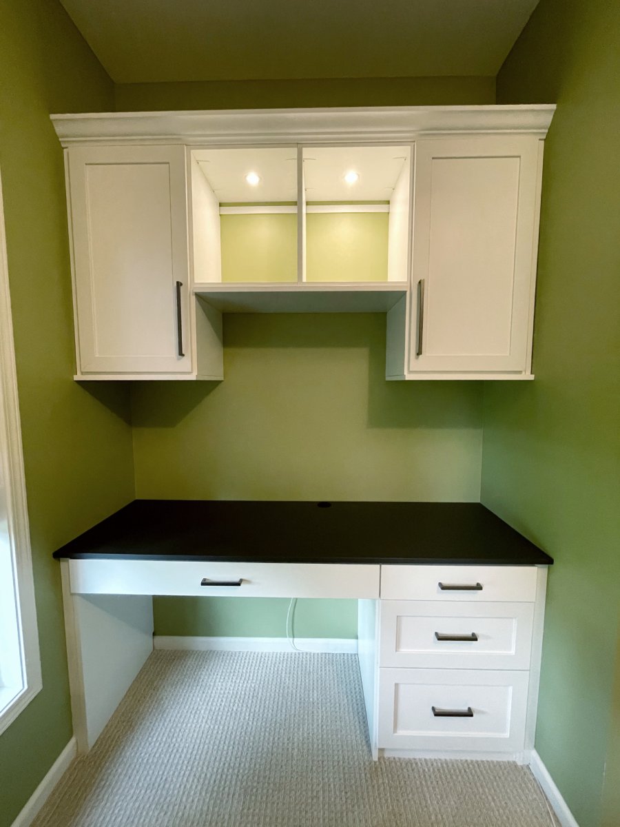 White desk with black countertop, drawers, and cabinets against green walls in a small room.