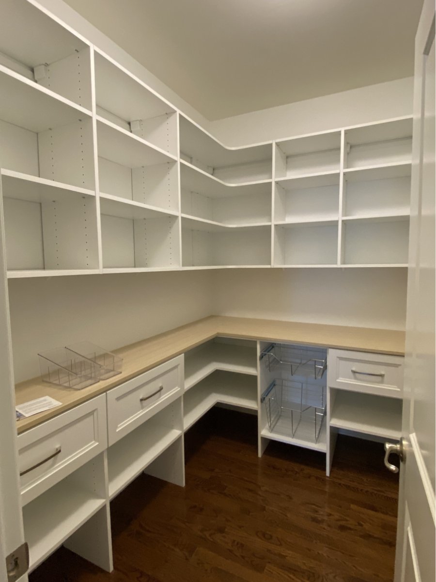 A walk-in pantry with white shelves, drawers, wooden countertop, and dark hardwood floors.