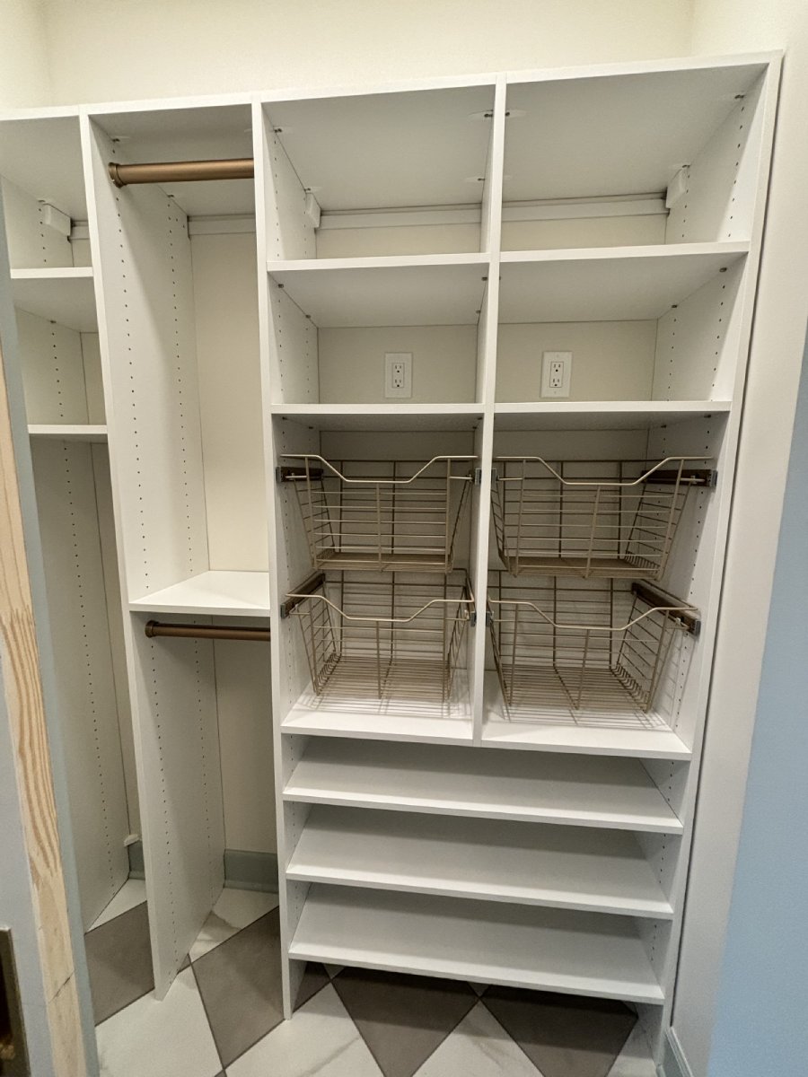 White closet shelves with wire baskets, open cubbies, and two hanging rods in a corner space.