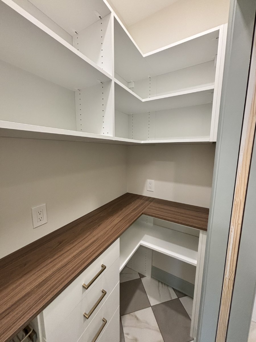 Walk-in pantry with white shelves, wood countertop, drawers, and patterned tile floor.