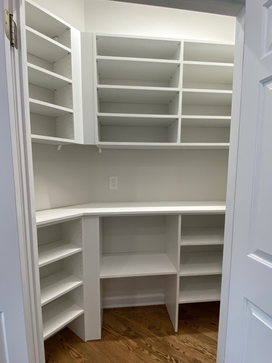 White pantry with empty shelves and hardwood floor, viewed through an open doorway.