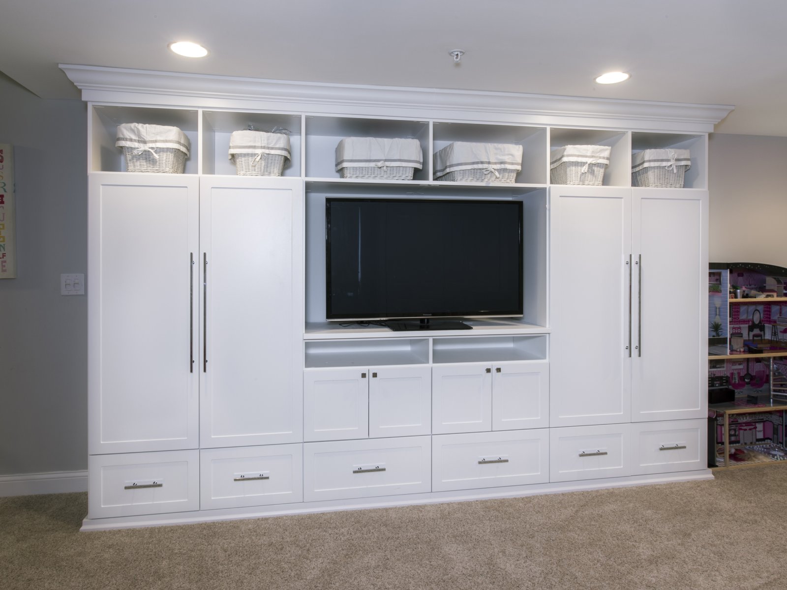 White built-in entertainment center with a TV, cabinets, drawers, and baskets on upper shelves.