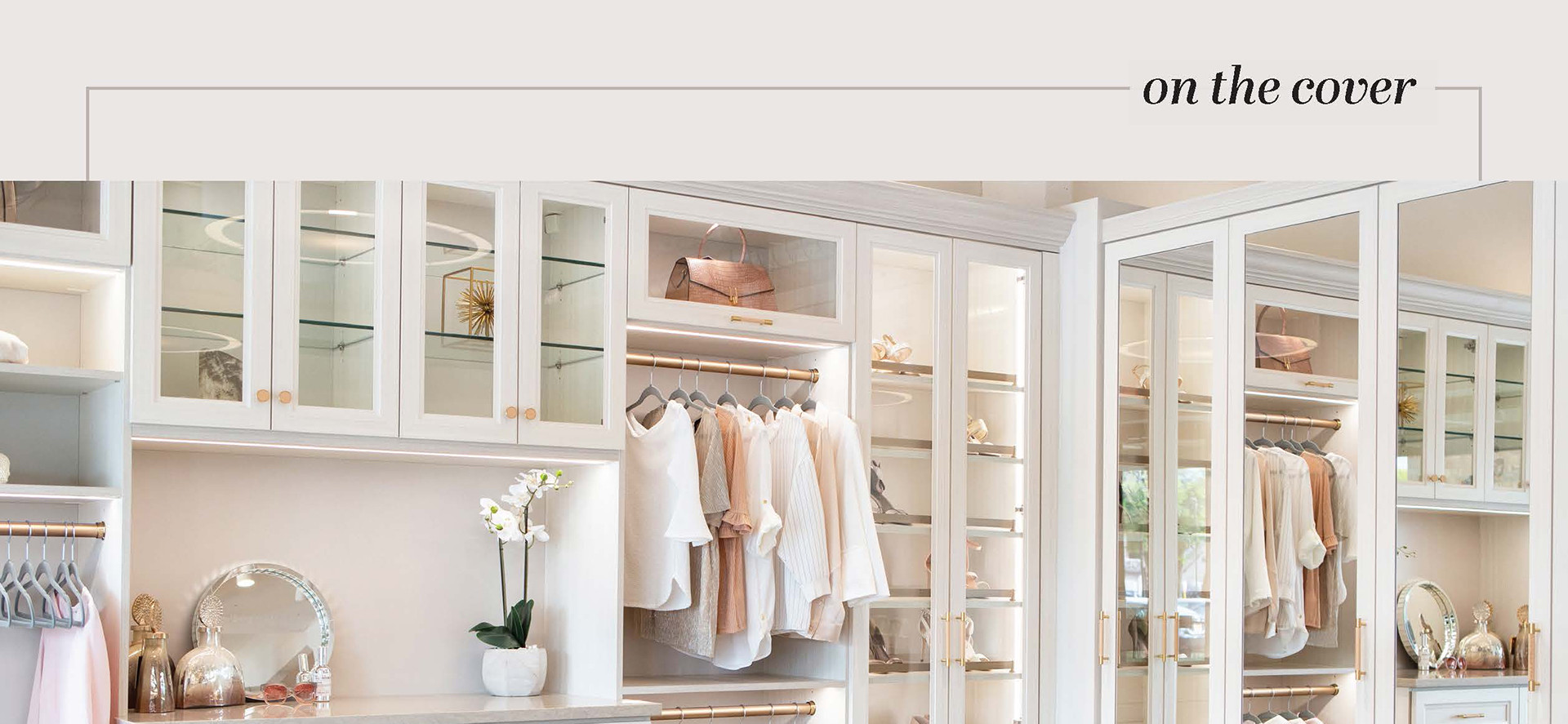 Bright, organized walk-in closet with glass cabinets, hanging clothes, and a vanity mirror.