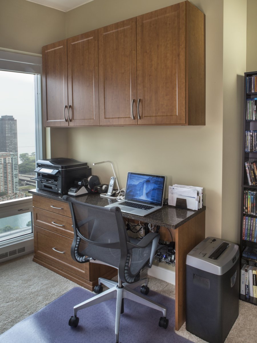 Modern home office with a laptop, printer, office chair, and storage cabinets near a window.