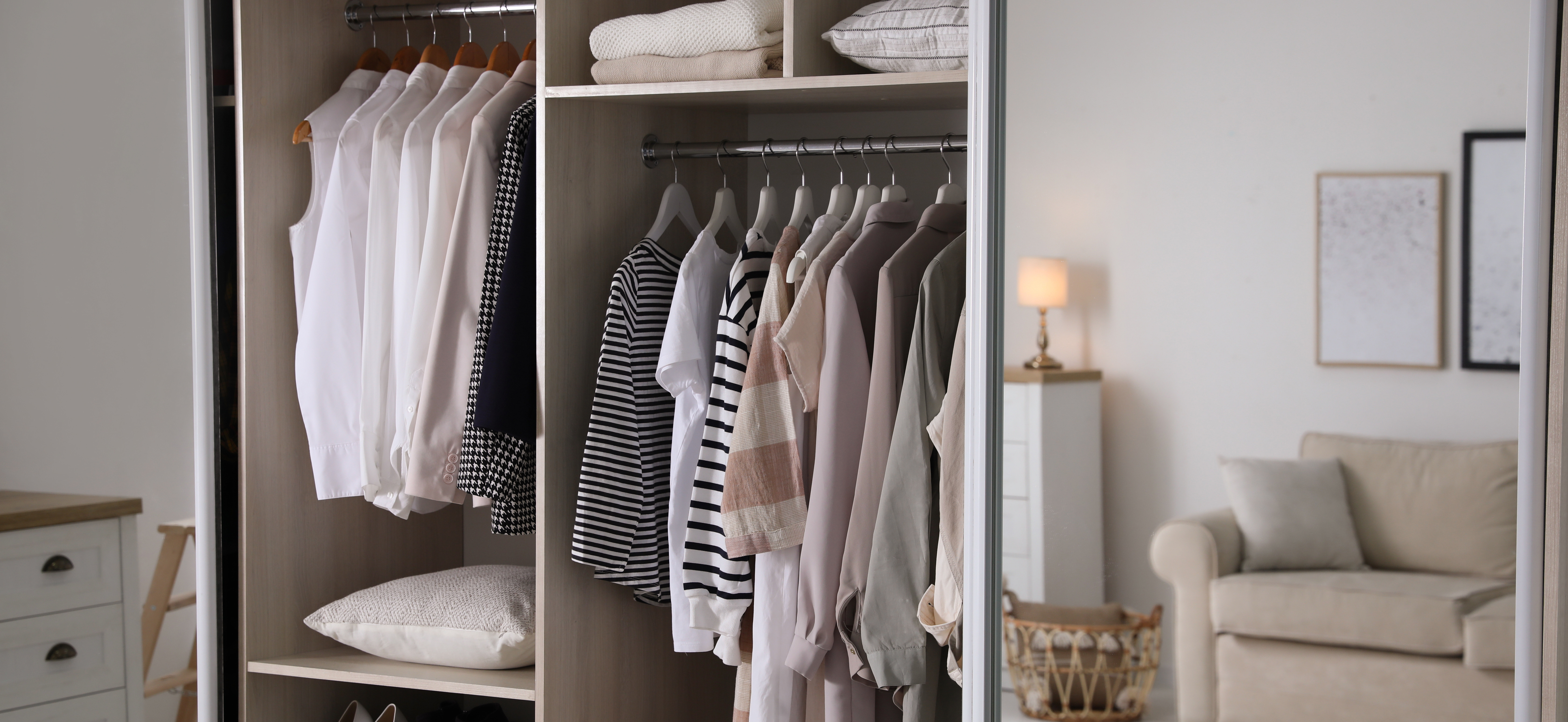 Open wardrobe with neatly hung shirts and sweaters, shelves holding folded clothes, cozy room.