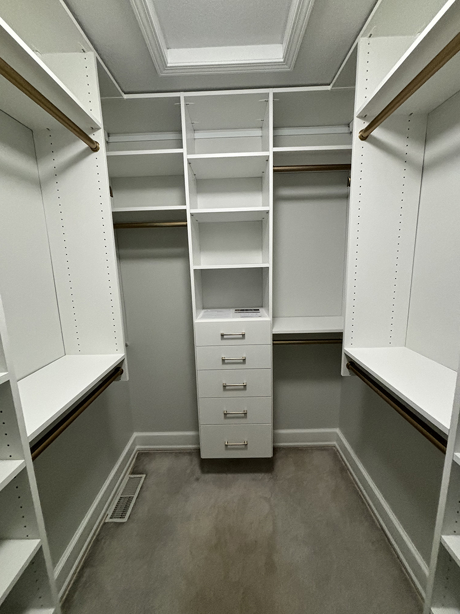 White walk-in closet with shelves, drawers, and hanging rods, and a vent on the floor.