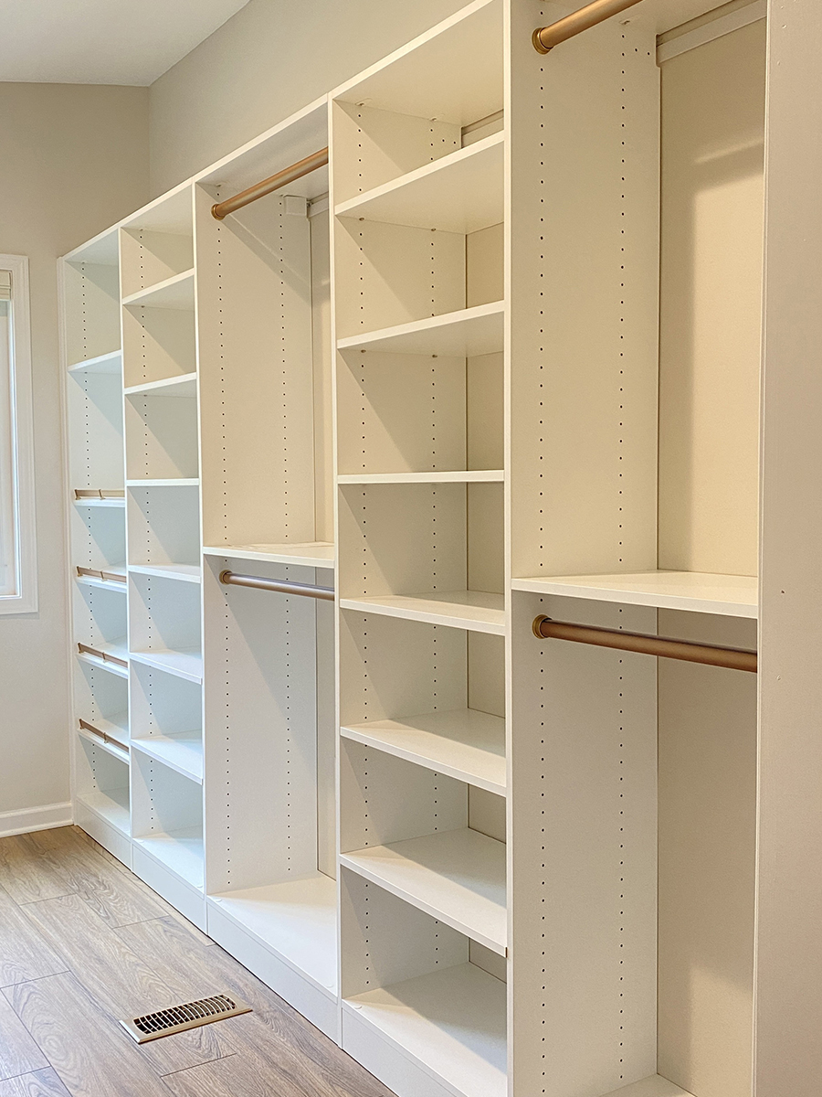 White built-in closet shelves and hanging rods in an empty, well-lit room with wood flooring.