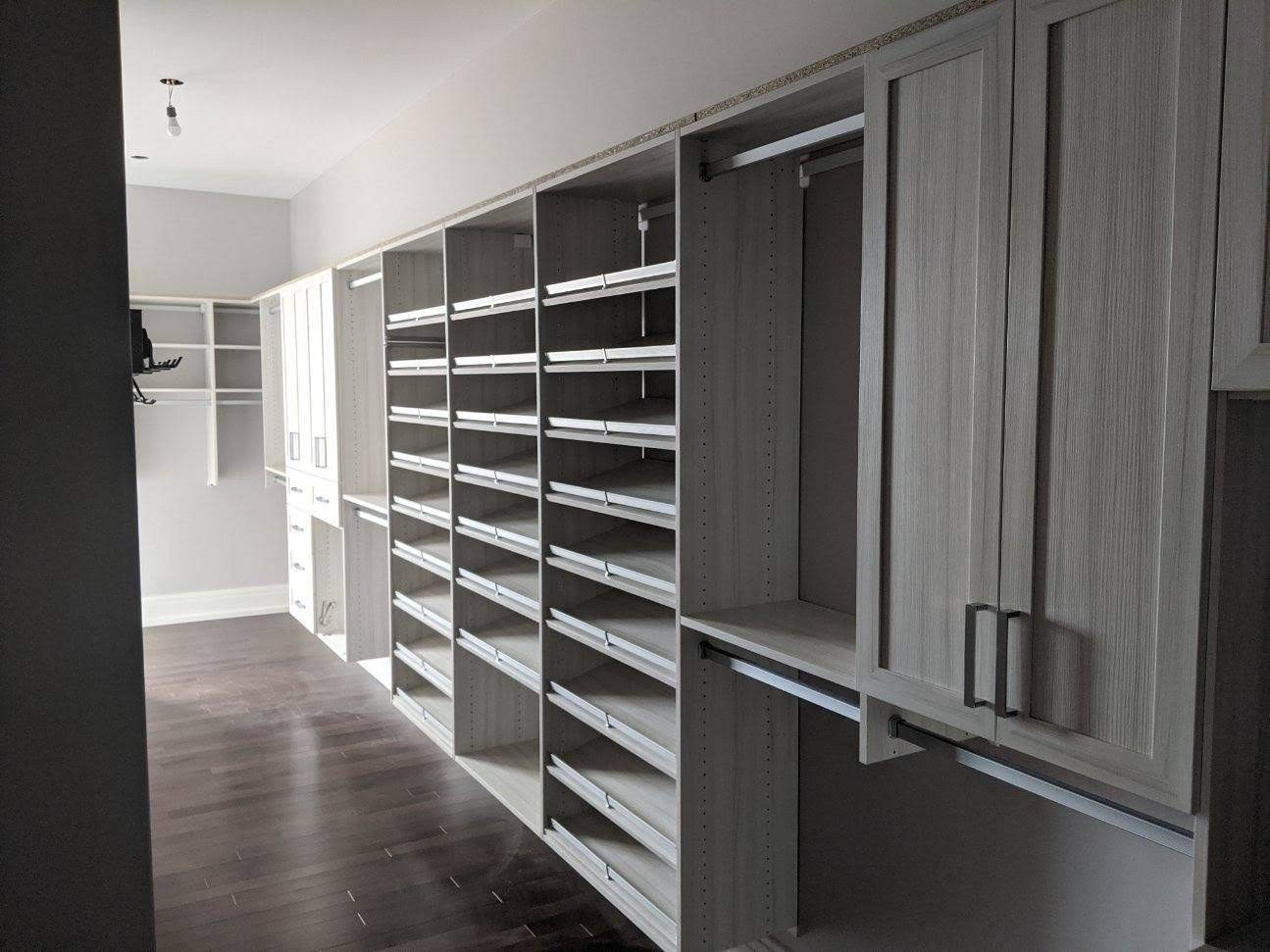Spacious walk-in closet with empty shelves, cabinets, and hanging rods along both walls.