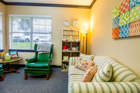 Cozy living room with striped sofa, green armchair, bookshelf, and colorful wall art.