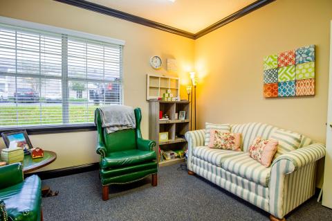 Cozy room with striped couch, green armchair, bookshelf, and window with blinds.