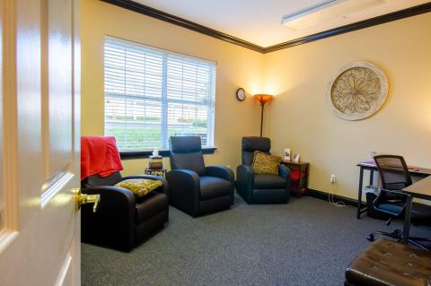 Cozy office with armchairs, a desk, bright window, and warm lighting.