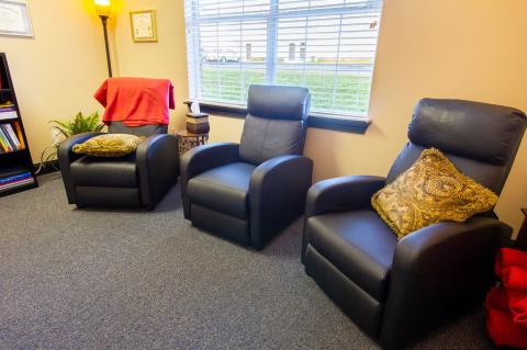 Three black armchairs with cushions are arranged in a cozy, well-lit room with a window.