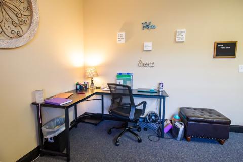 A tidy home office with a desk, chair, lamp, supplies, and motivational wall decor.