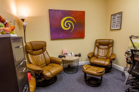 Two brown leather chairs in a cozy office with colorful art and a motivational sign on the wall.