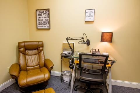 A cozy home office with a brown recliner, desk, microphone, lamp, and motivational posters.