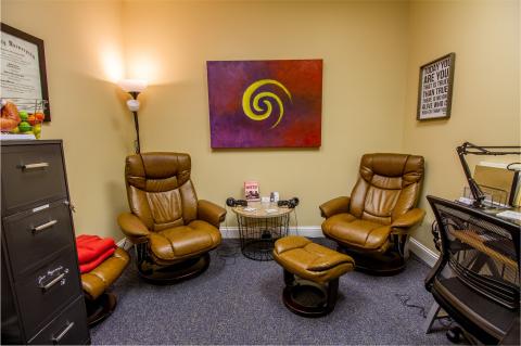 Two brown recliners with a matching ottoman in a cozy office with wall art and soft lighting.