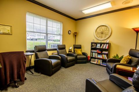 Cozy office with four black chairs, bookshelves, window, and warm lighting.