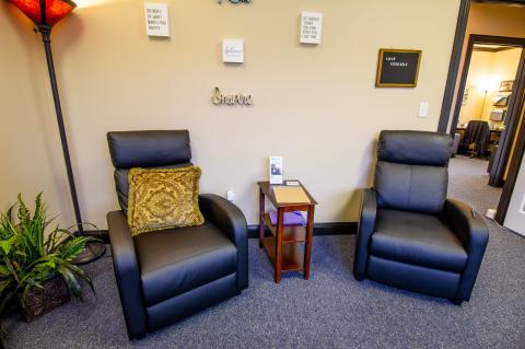 Two black recliners with a small table between them in a cozy, warmly lit office space.