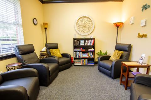 Cozy room with four black recliners, bookshelf, lamps, and decorative wall art.