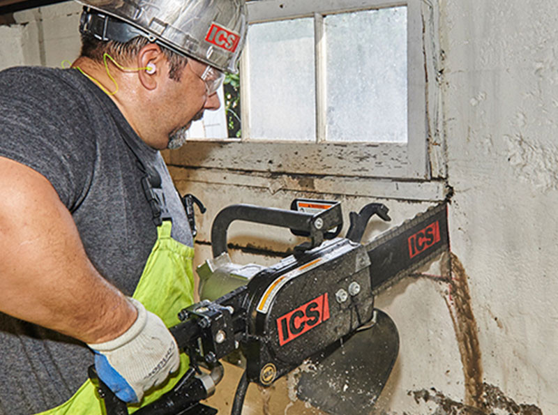 Man in hard hat cutting through concrete wall with ICS chainsaw