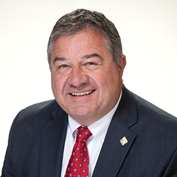 Smiling man in a suit and tie against a light gray background.