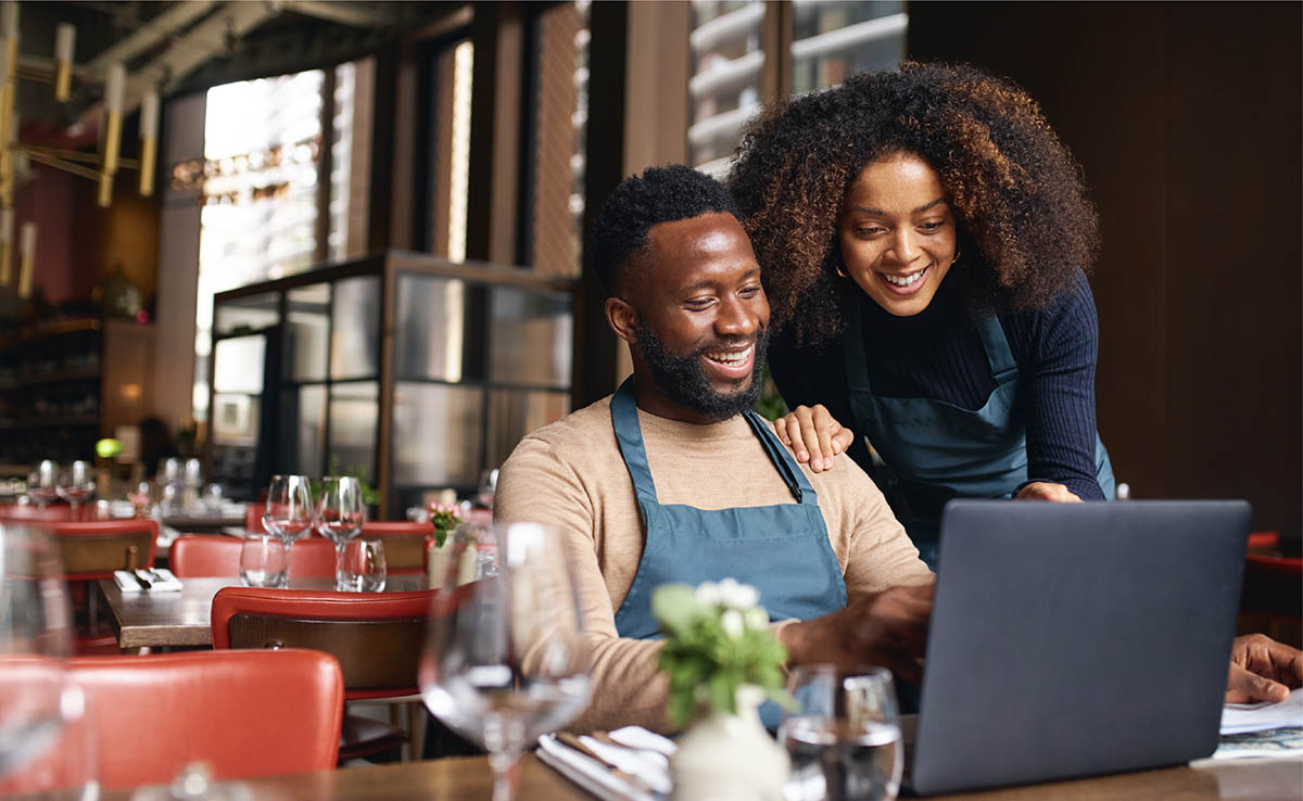A man and woman in aprons looking at a laptop screen together.