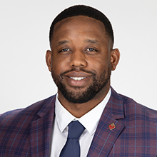 Man wearing a plaid suit jacket, white shirt, and navy tie, smiling at the camera.
