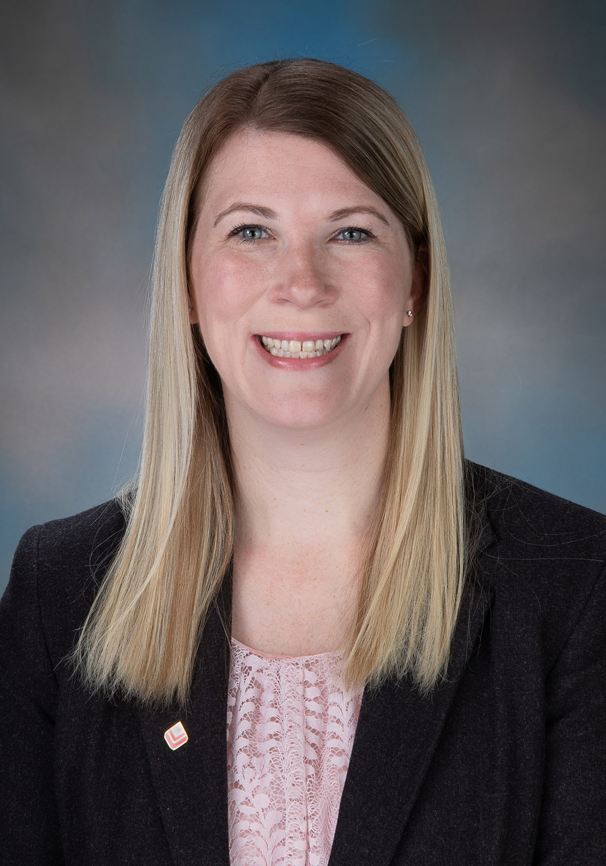 Smiling woman with straight brown hair, wearing a black blazer and polka dot blouse.